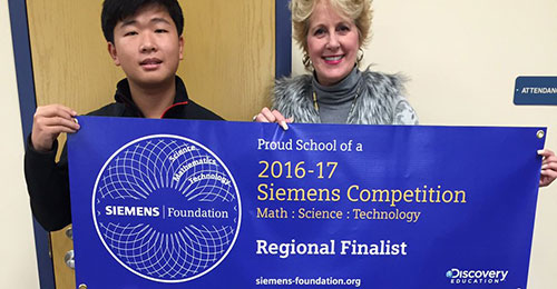 Yoshihiro holding up a scholarship banner: Proud school of a 2016-17 Siemens Competition Regional Finalist
