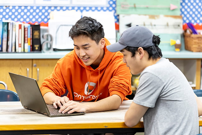Two students collaborating over a laptop.
