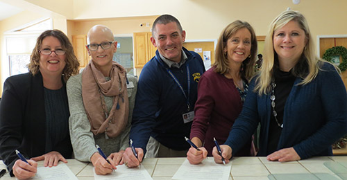 Group photo of school and partnership representatives signing agreement.
